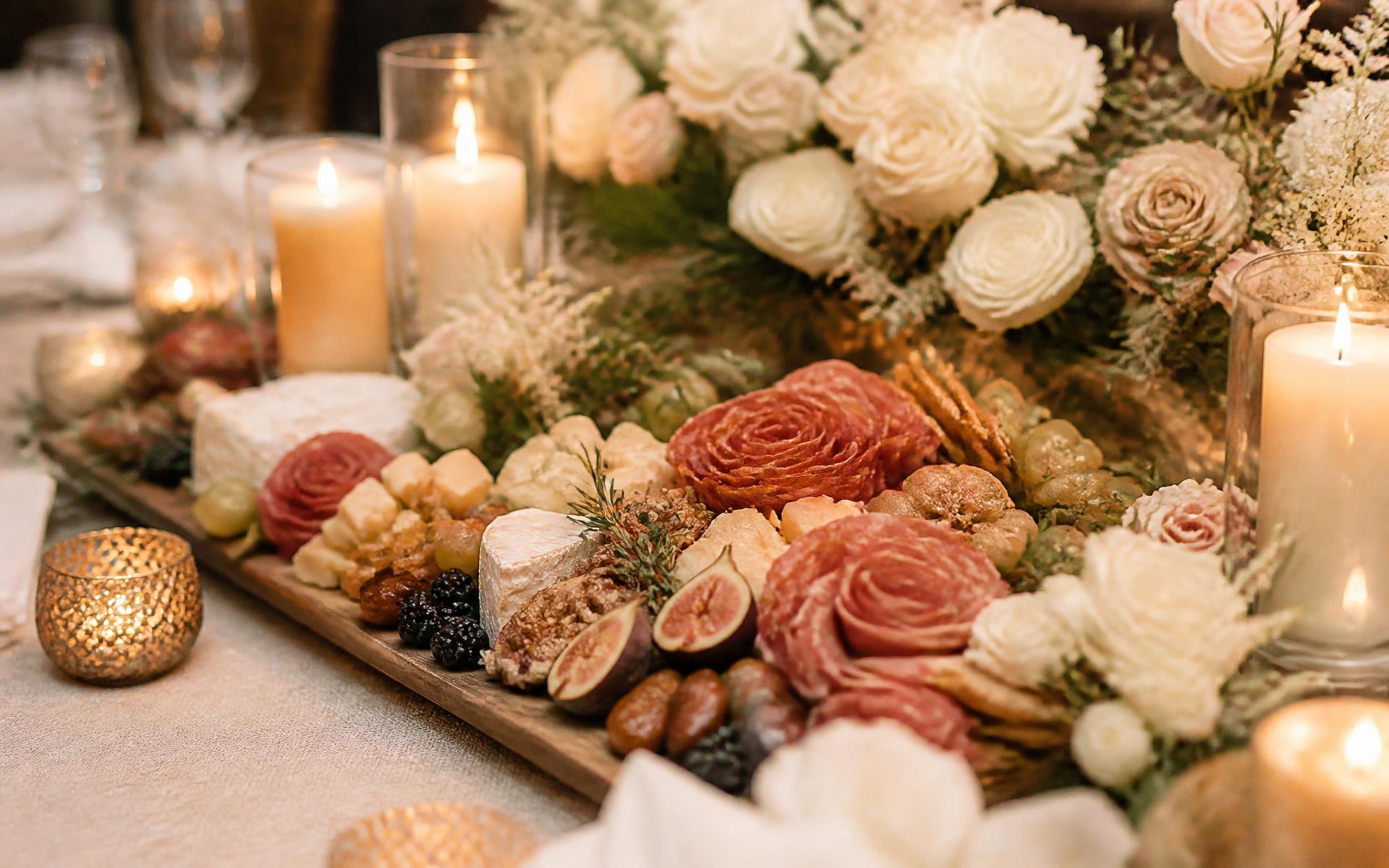 Candlelit close-up of a refined charcuterie board with flowers, figs and cured meats
